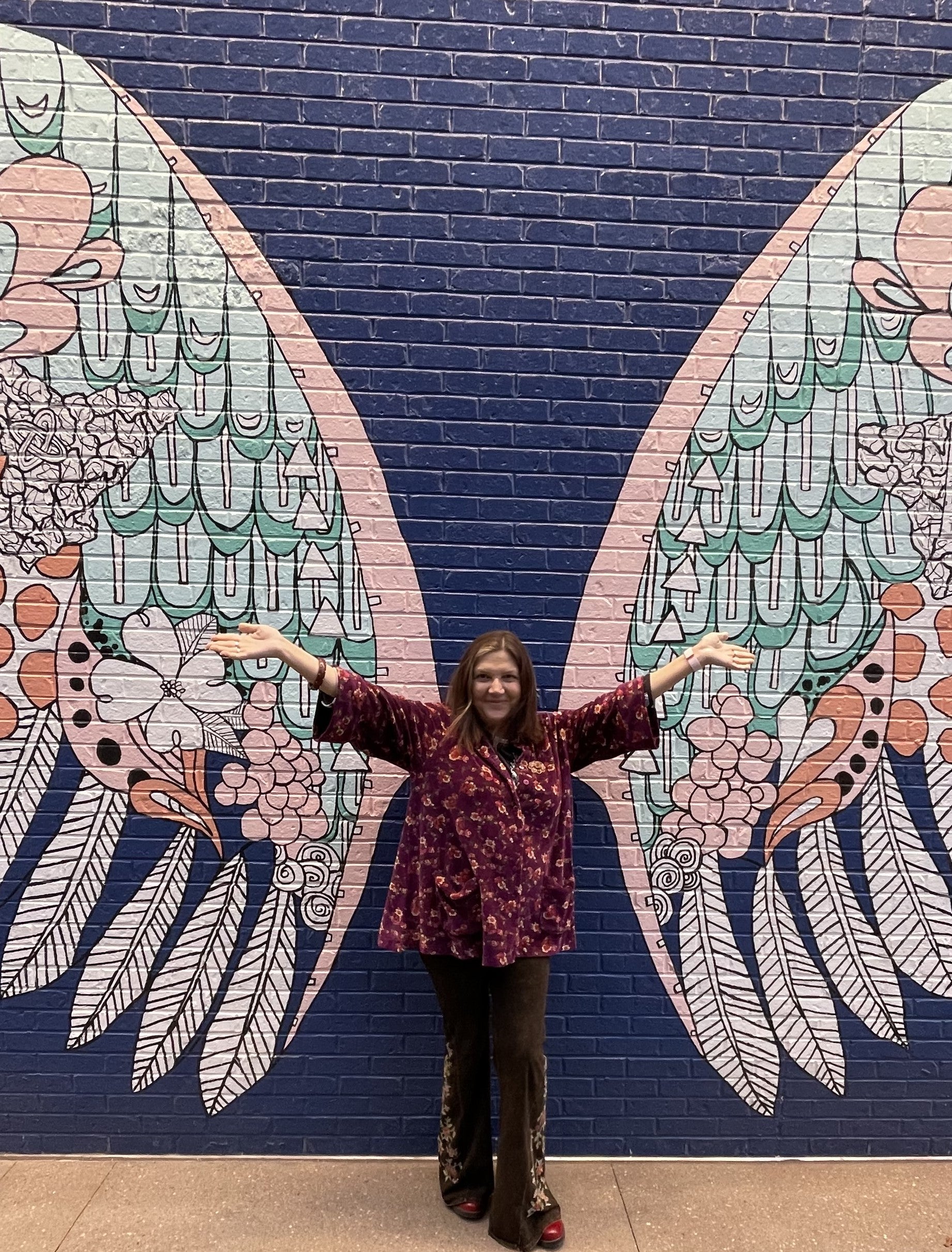 A picture of Mandianne with her arms outstretched with wings painted on a brick wall.