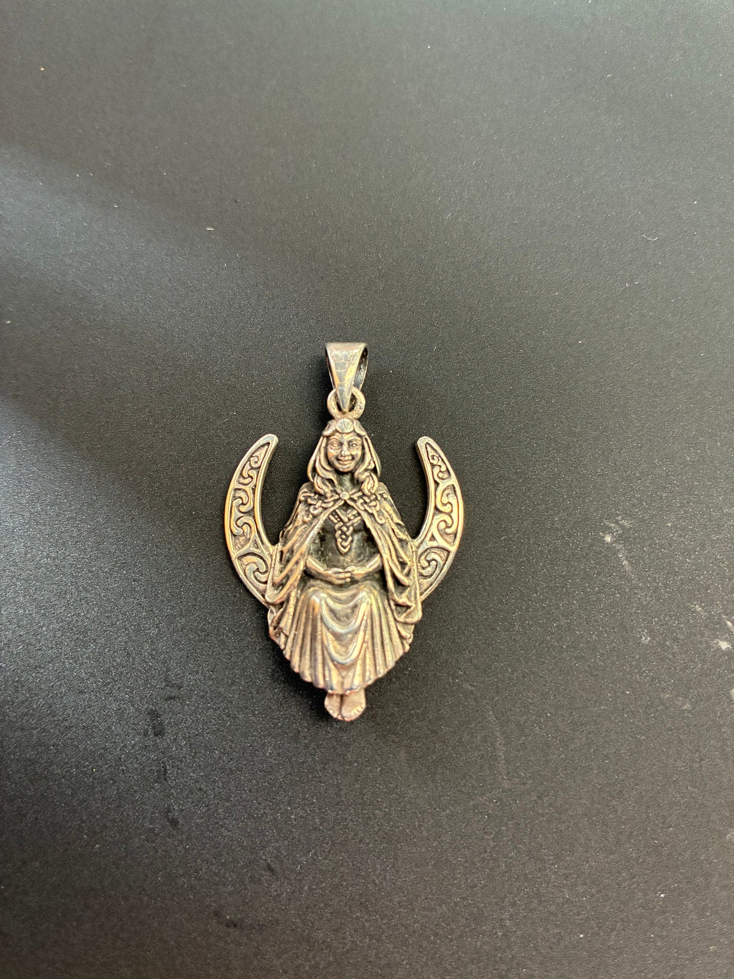 A sterling silver Goddess figure sitting on a crescent moon.
