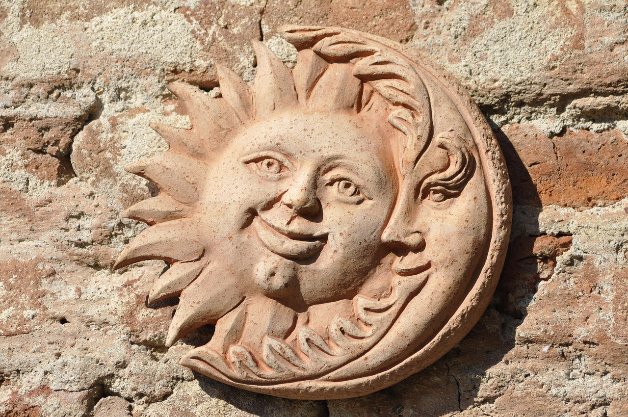 Decorative stone wall plaque with sun and moon design on a textured wall.