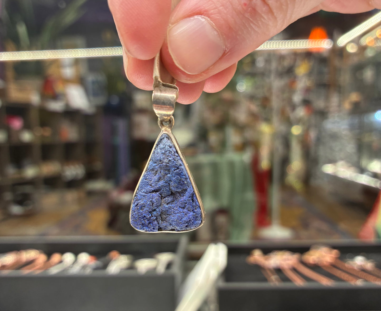 Hand holding a blue pendant with a blurred store background