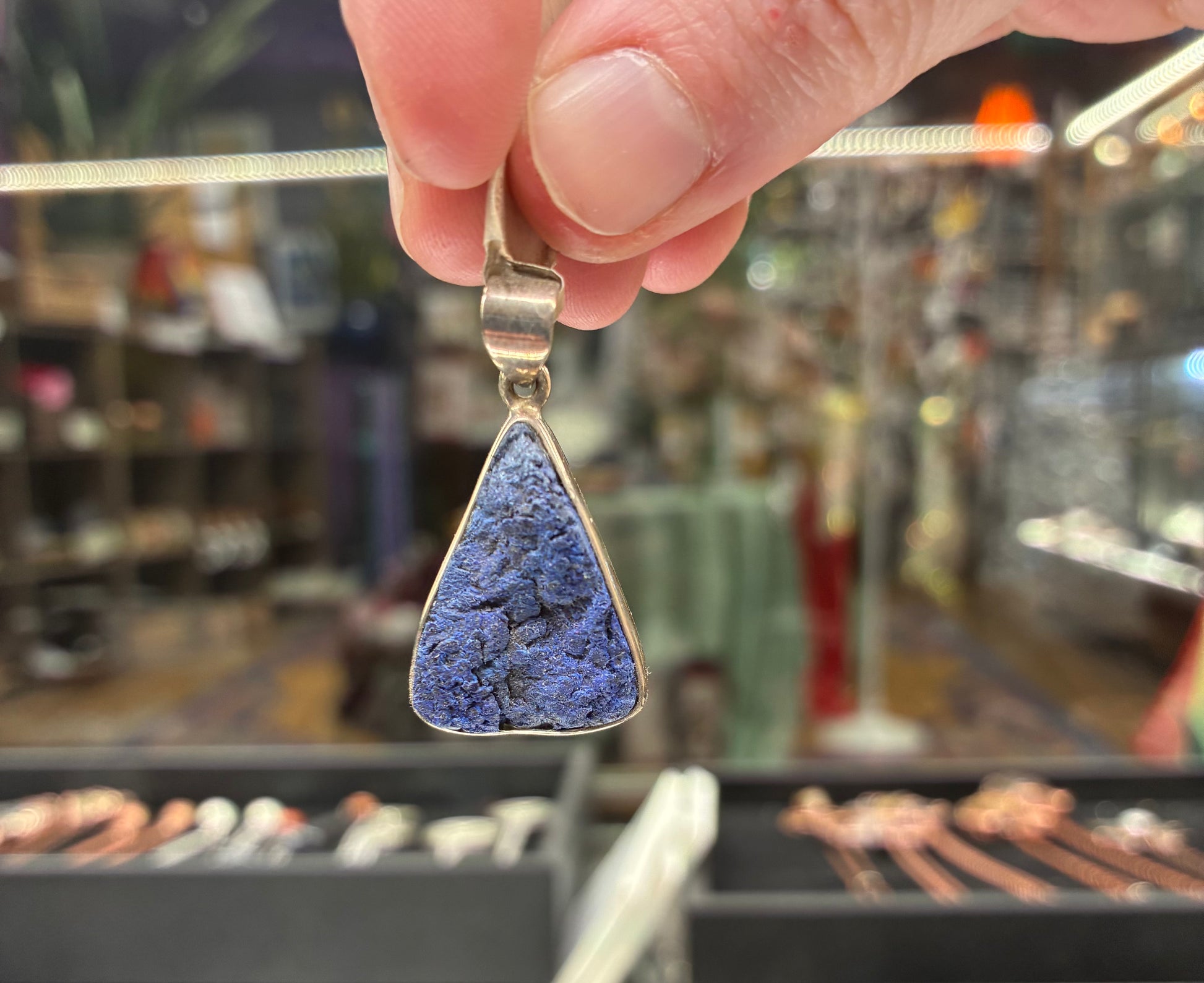 Hand holding a blue pendant with a blurred store background