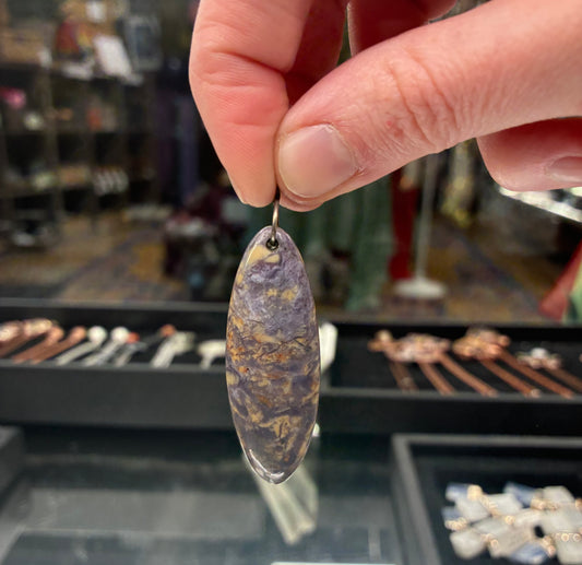 Hand holding a purple and gold pendant with a jewelry store in the background
