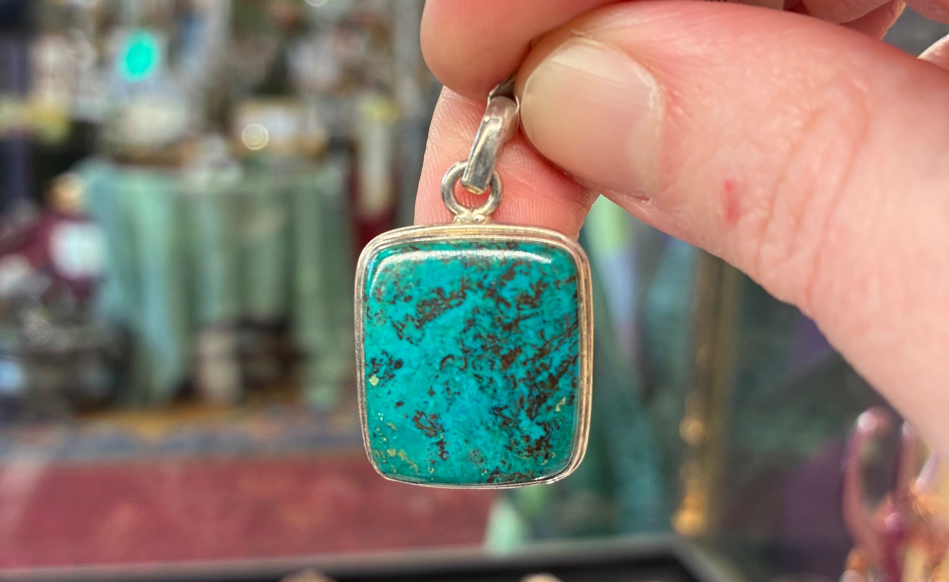 Turquoise pendant with silver setting held by a hand against a blurred background