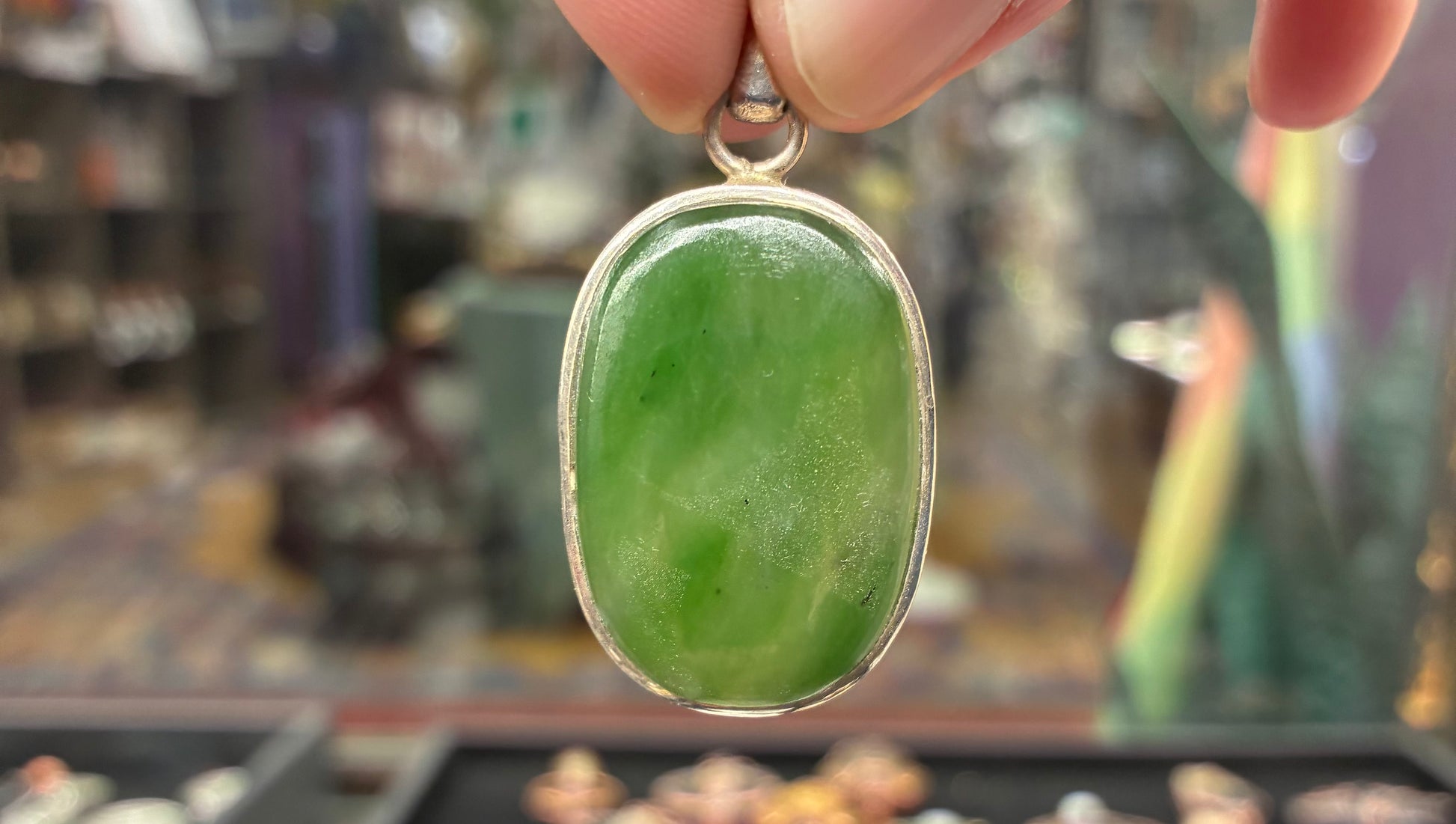 Green pendant with silver frame held by a hand against a blurred background