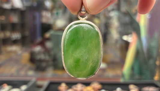 Green pendant with silver frame held by a hand against a blurred background
