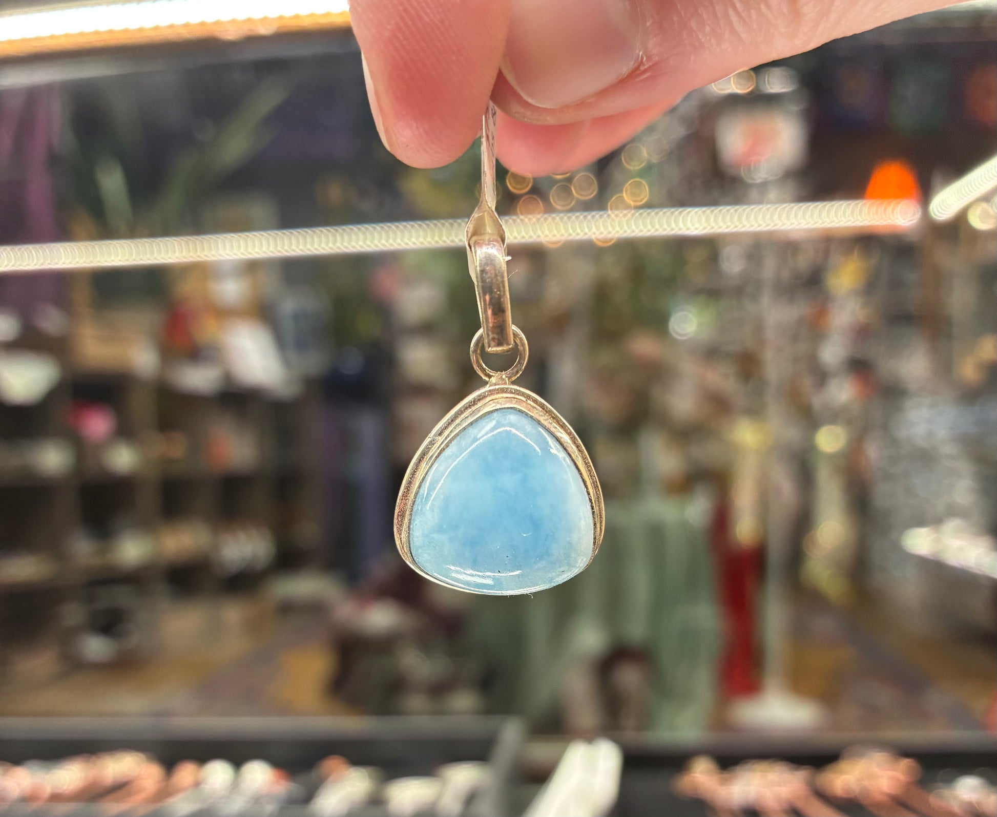 Hand holding a blue teardrop pendant with a blurred store background