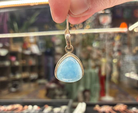 Hand holding a blue teardrop pendant with a blurred store background