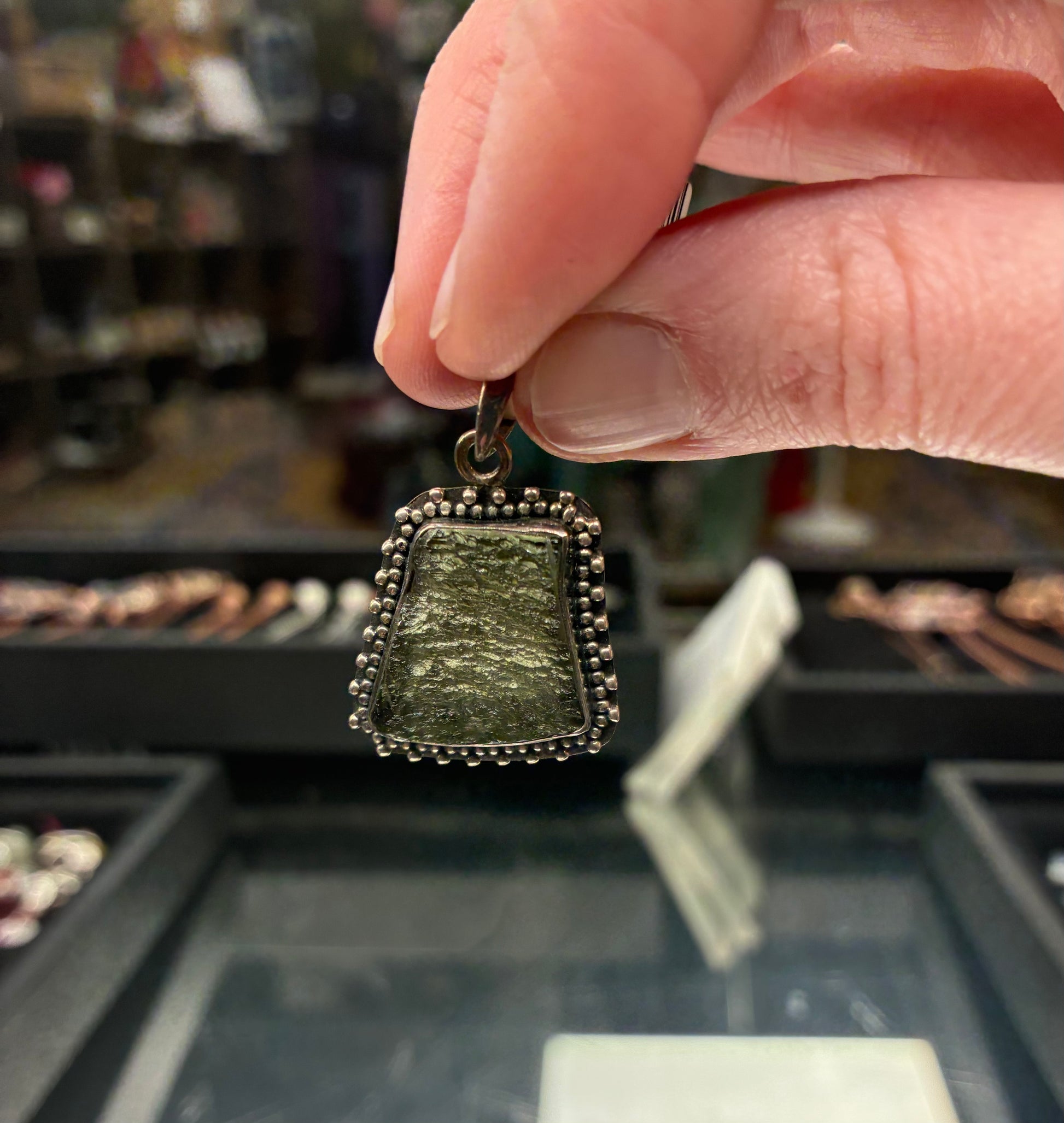 Hand holding a green stone pendant with a blurred jewelry store background