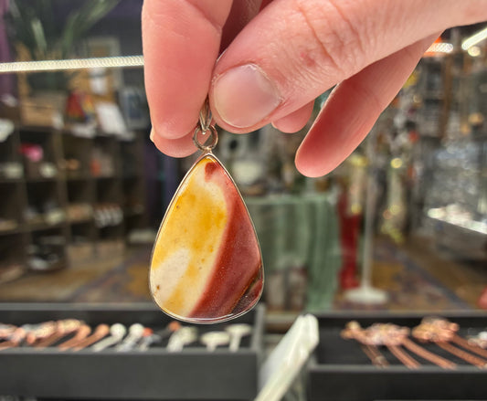 Teardrop-shaped pendant with a marbled design held by a hand in a jewelry store.