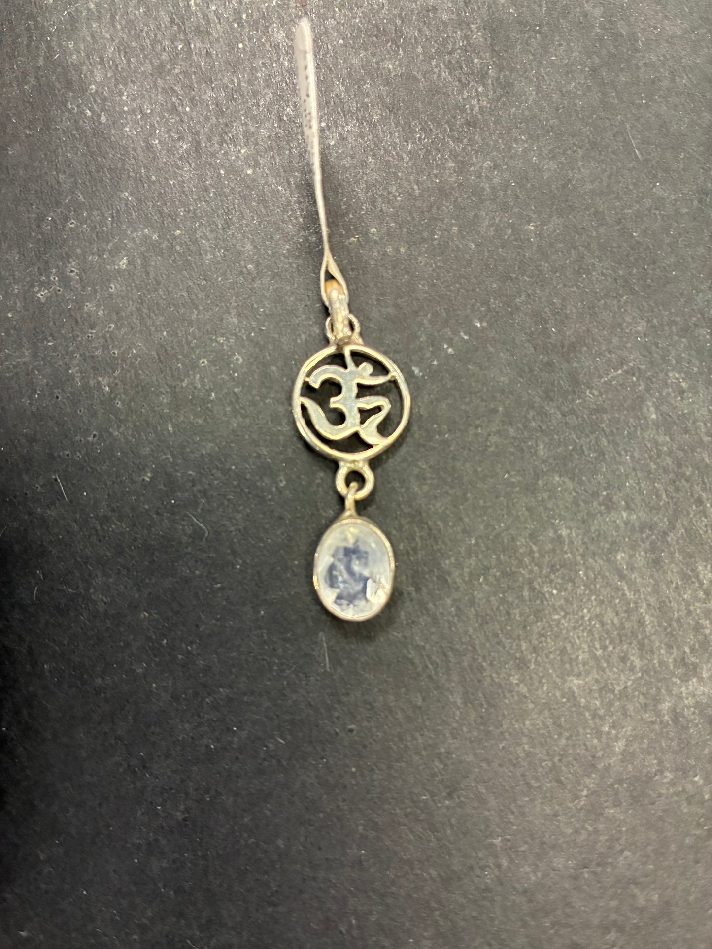 Jewelry pendant with Om symbol and blue stone on a dark background