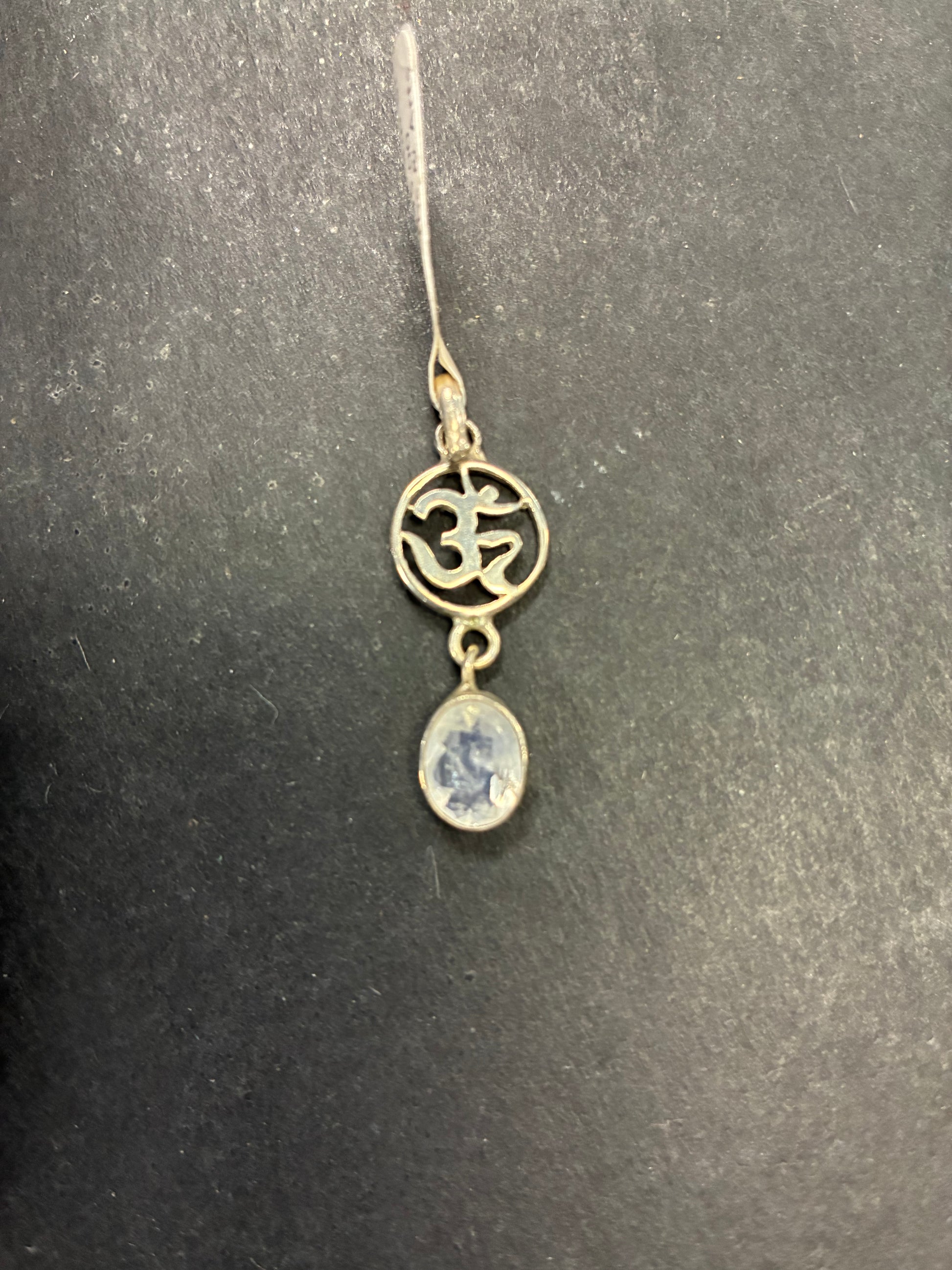 Jewelry pendant with Om symbol and blue stone on a dark background