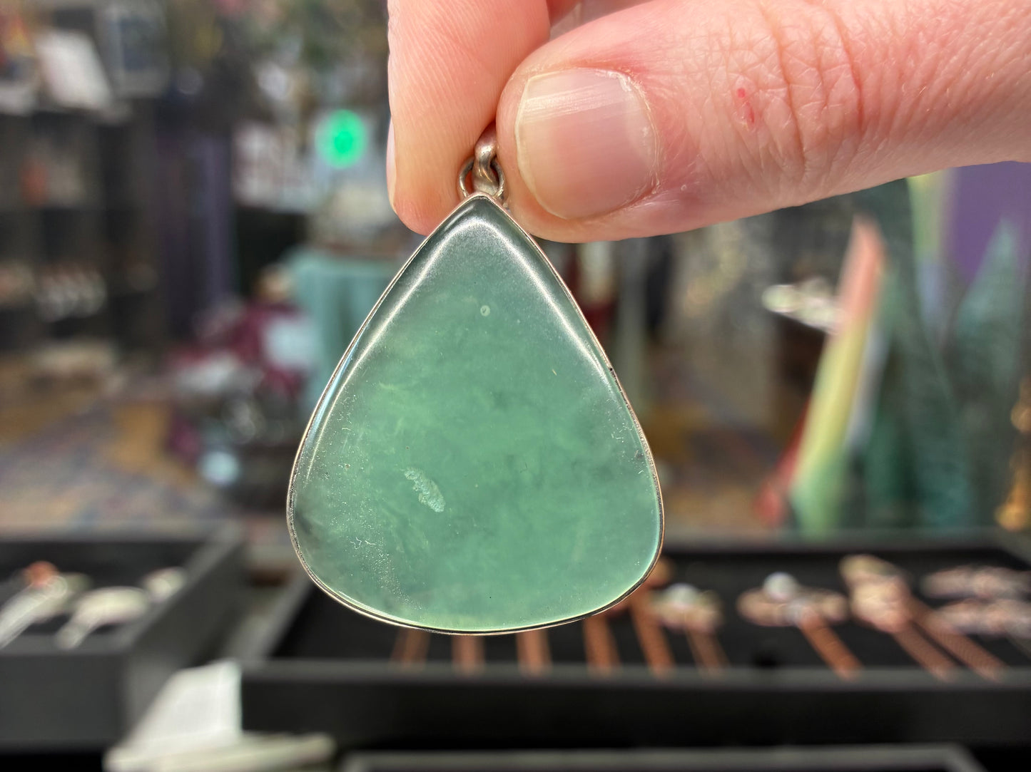 Hand holding a green teardrop-shaped pendant with a blurred store background