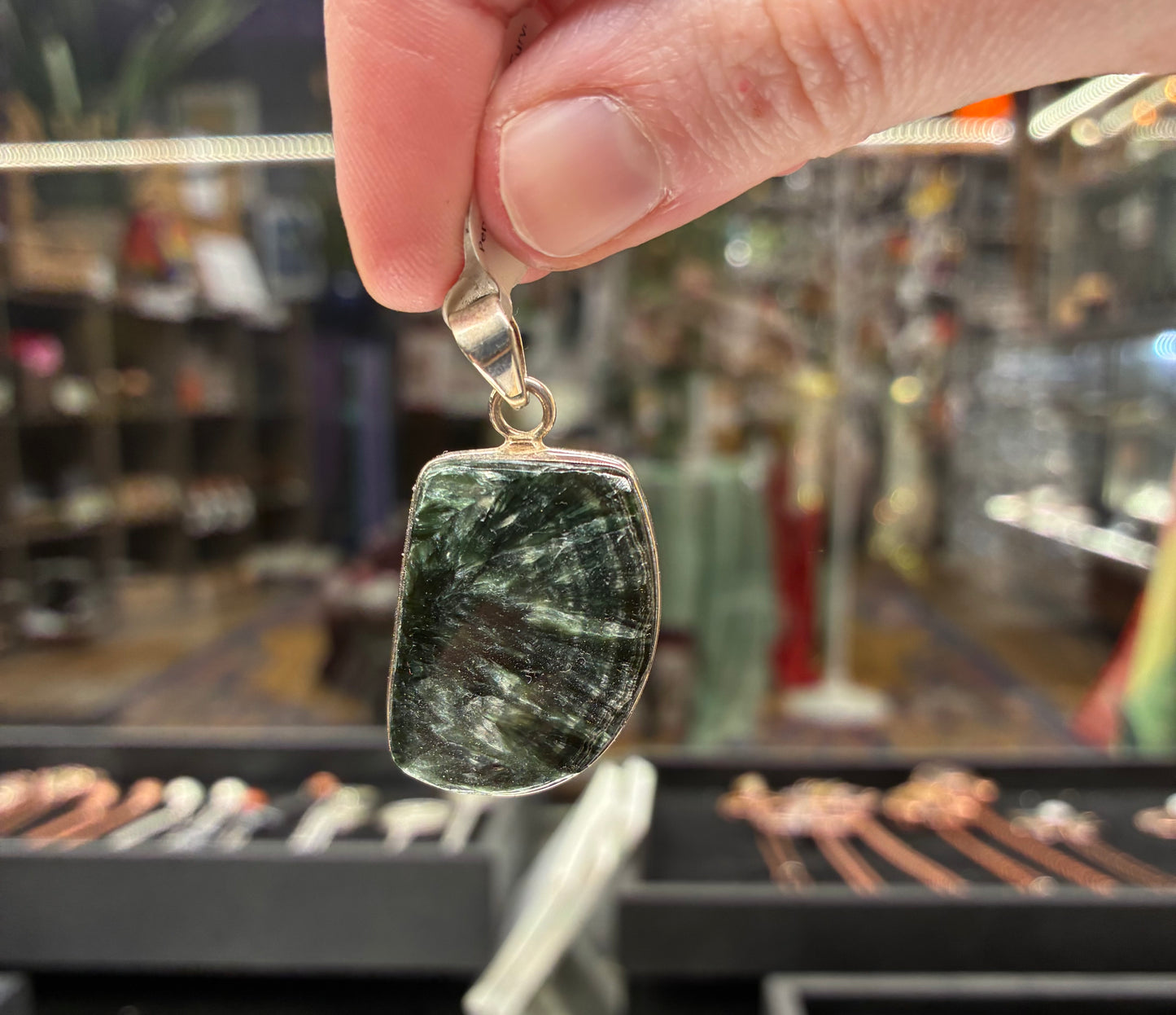 Hand holding a pendant with a green stone in a store setting