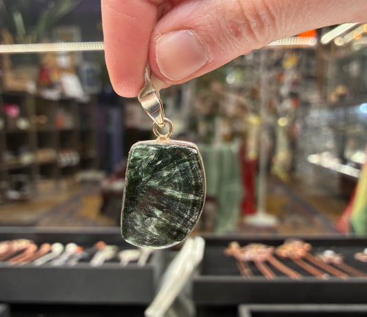 Hand holding a pendant with a green stone in a store setting