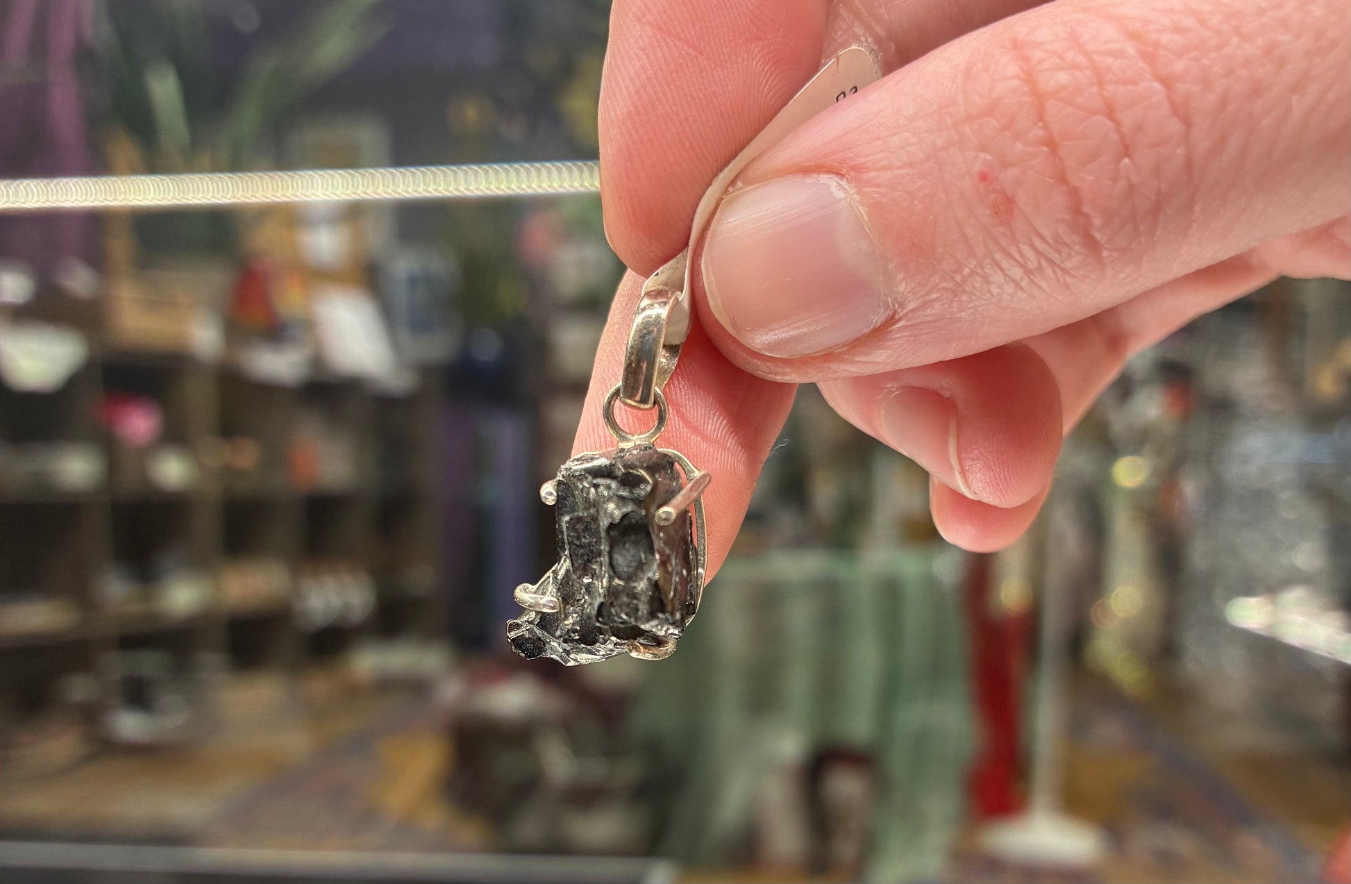 Hand holding a silver pendant with a dark stone against a blurred store background