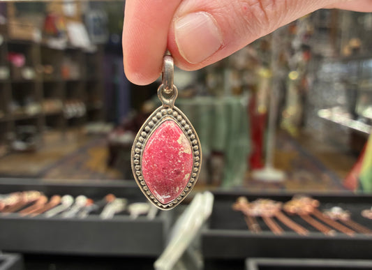 Pink stone pendant held by a hand with a blurred store background