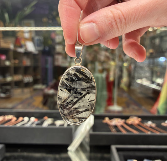 Hand holding a silver pendant with a textured design against a blurred store background