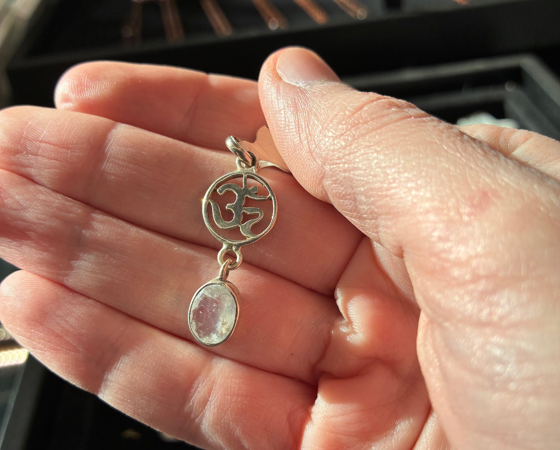 Hand holding a silver pendant with a stone