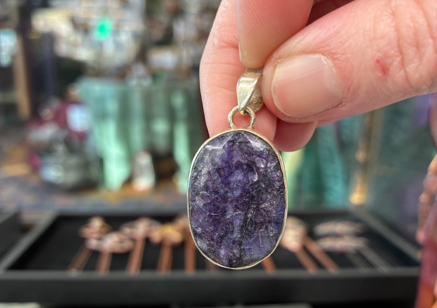 Hand holding a purple pendant with a blurred jewelry store background