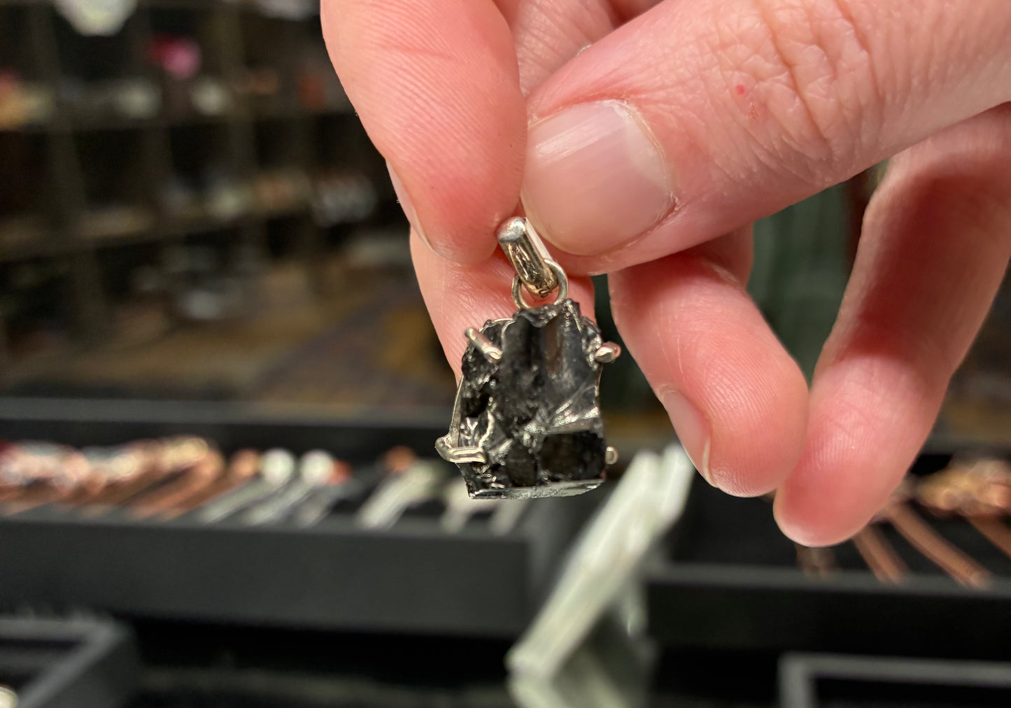 Hand holding a silver pendant with a mountain design against a blurred jewelry store background