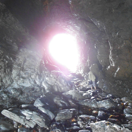 A person standing inside a rocky cave or tunnel with a bright white light glowing from the opening in the distance.