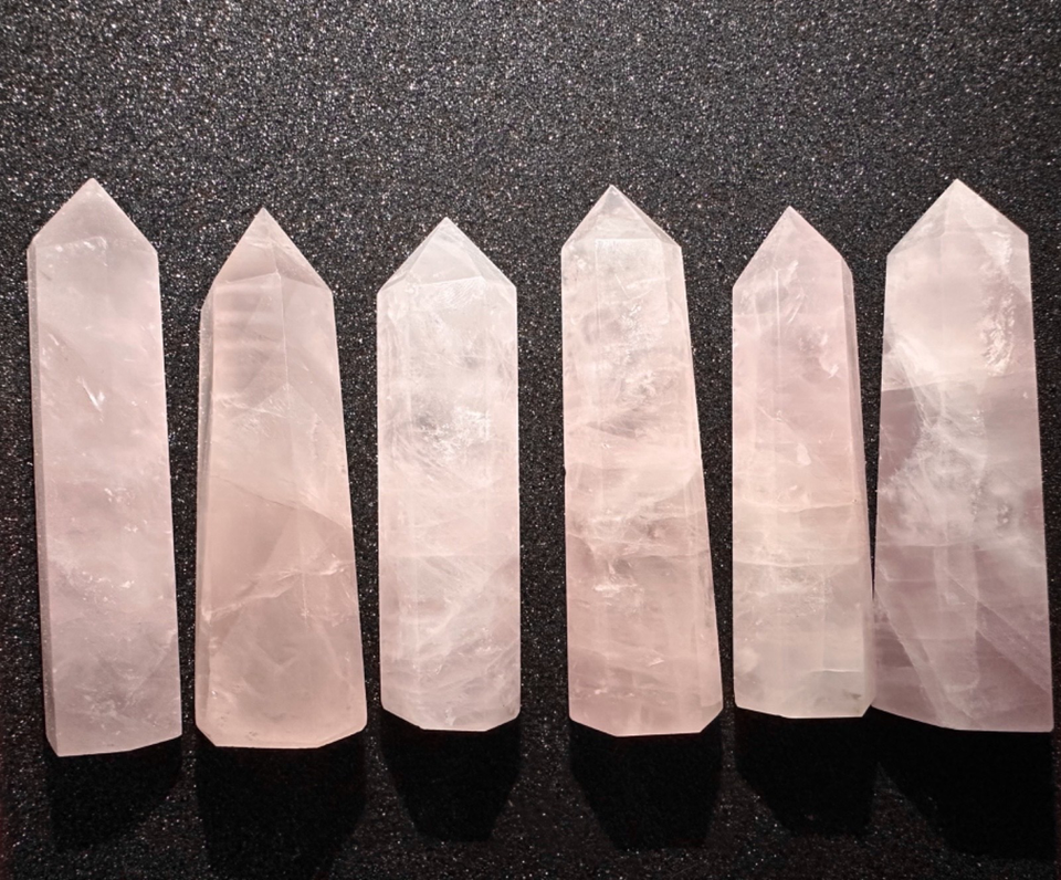 Six pale pink rose quartz crystal points arranged in a row on a dark textured background.