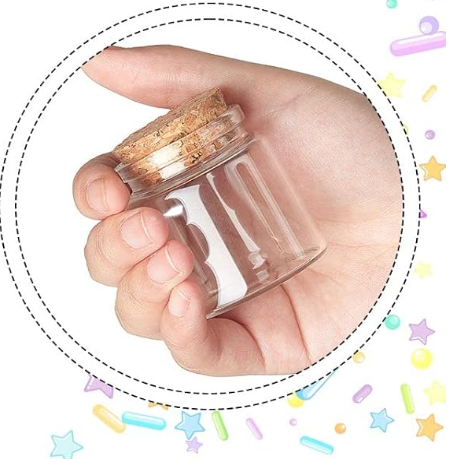 Hand holding a small clear glass jar with a cork lid against a white background