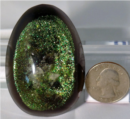 Oval-shaped green gemstone next to a quarter for scale on a white background
