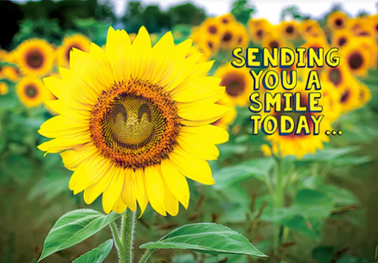 A close-up sunflower in a field with other sunflowers blurred in the background, overlaid with the text 'SENDING YOU A SMILE TODAY.