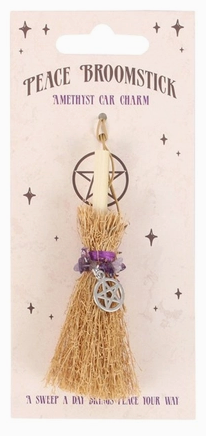 A 'Peace Broomstick' amethyst car charm by Mystick, featuring a natural wood broomstick handle, tan straw bristles, a purple amethyst band, and a silver pentagram charm, all mounted on a pink backing card with star illustrations.