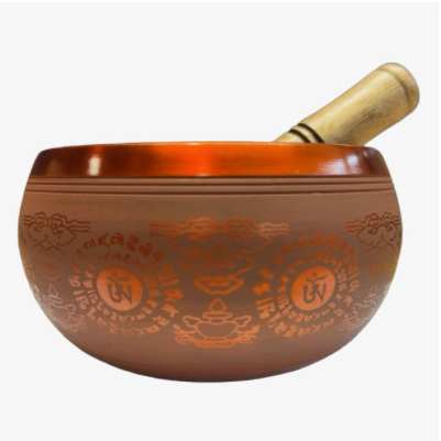 A Tibetan singing bowl made of bronze with etched Tibetan Buddhist symbols and a light wood striker, shown against a plain white background.