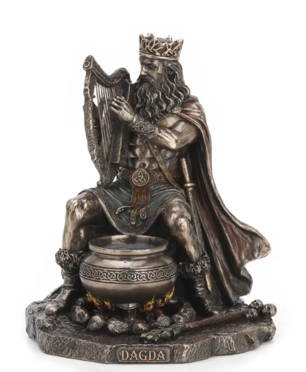 A detailed resin figurine of Dagda, the Irish king and harp player, seated on a rock base with a cauldron and flames. The figurine has a metallic antique finish with dark gray, bronze, and brown tones, and is set against a plain white background.