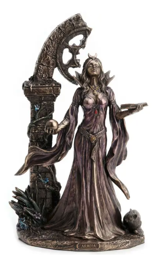 Aradia statue of a woman in a flowing dark gown standing beside a large stone archway, holding a tray and a skull, with a small creature at the base. The sculpture appears metallic bronze with purple undertones and small red and blue accents, shown on a plain white background.