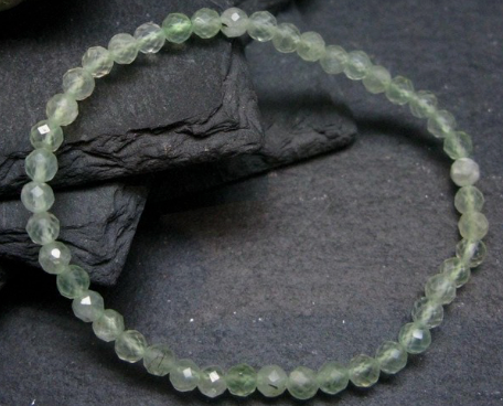 A beaded stretch bracelet made of faceted light green gemstone beads, displayed on a dark textured slate background.