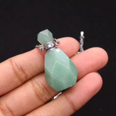 A faceted light green stone pendant or bottle stopper with silver metal caps, held in a person's hand against a dark background.