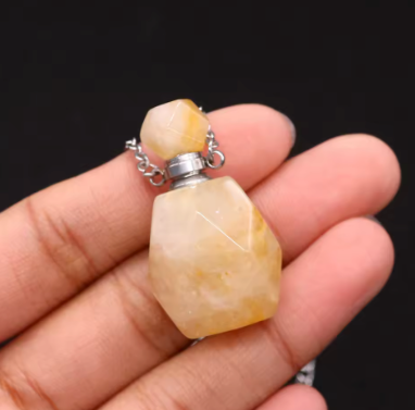 A faceted pale yellow stone pendant necklace held in a person's hand against a dark background.