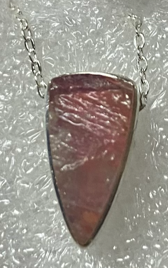 Triangular red stone pendant on a silver chain against a textured gray background