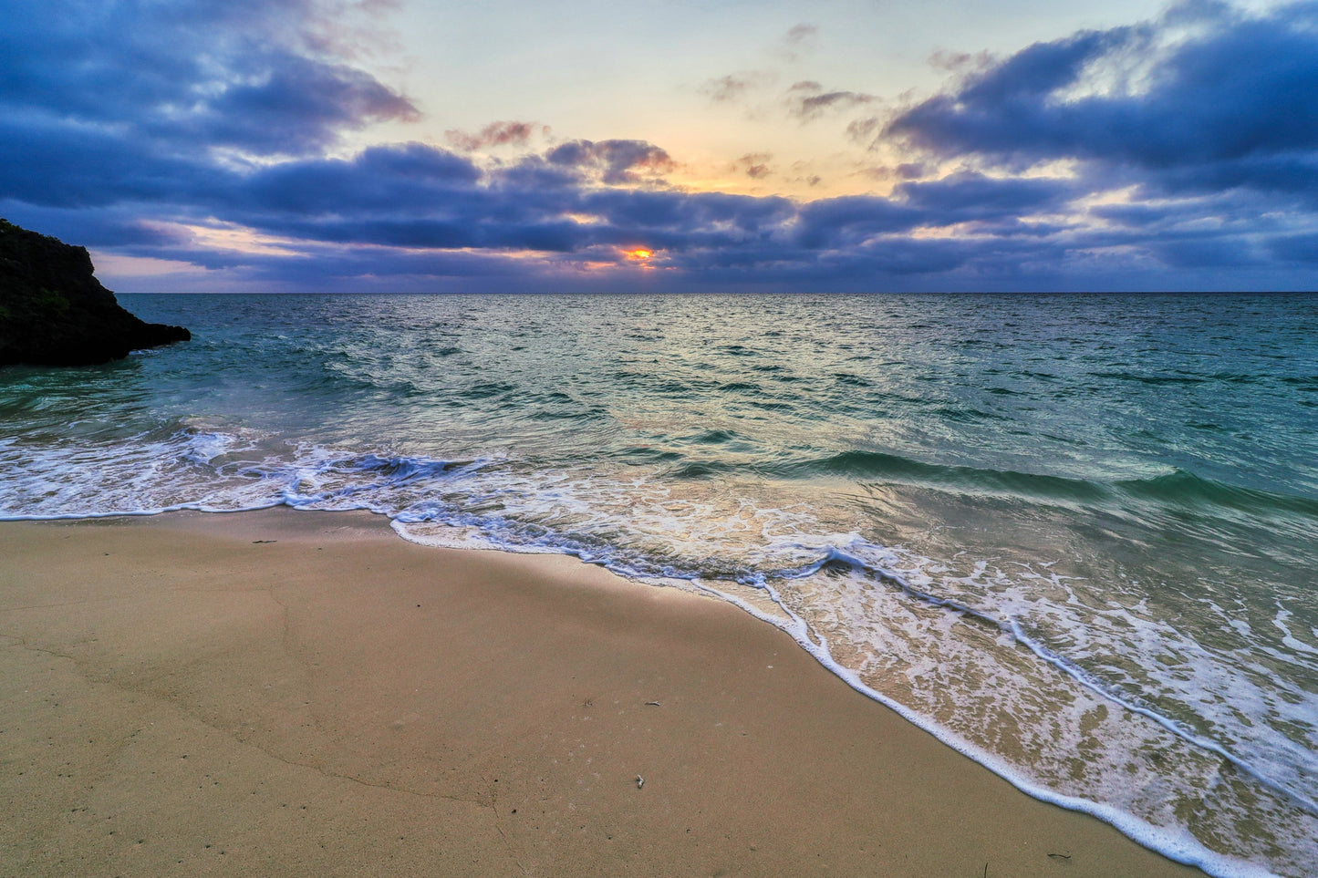 Beach scene with waves crashing onto the shore during sunset.
