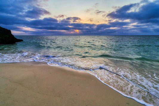 Beach scene with waves crashing onto the shore during sunset.