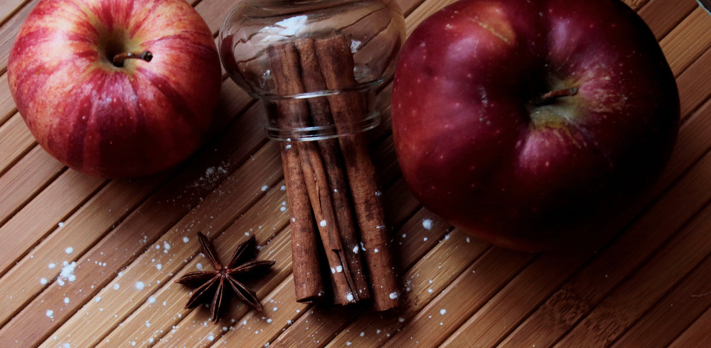 two apples on a wood table with cinnamon sticks and anise.
