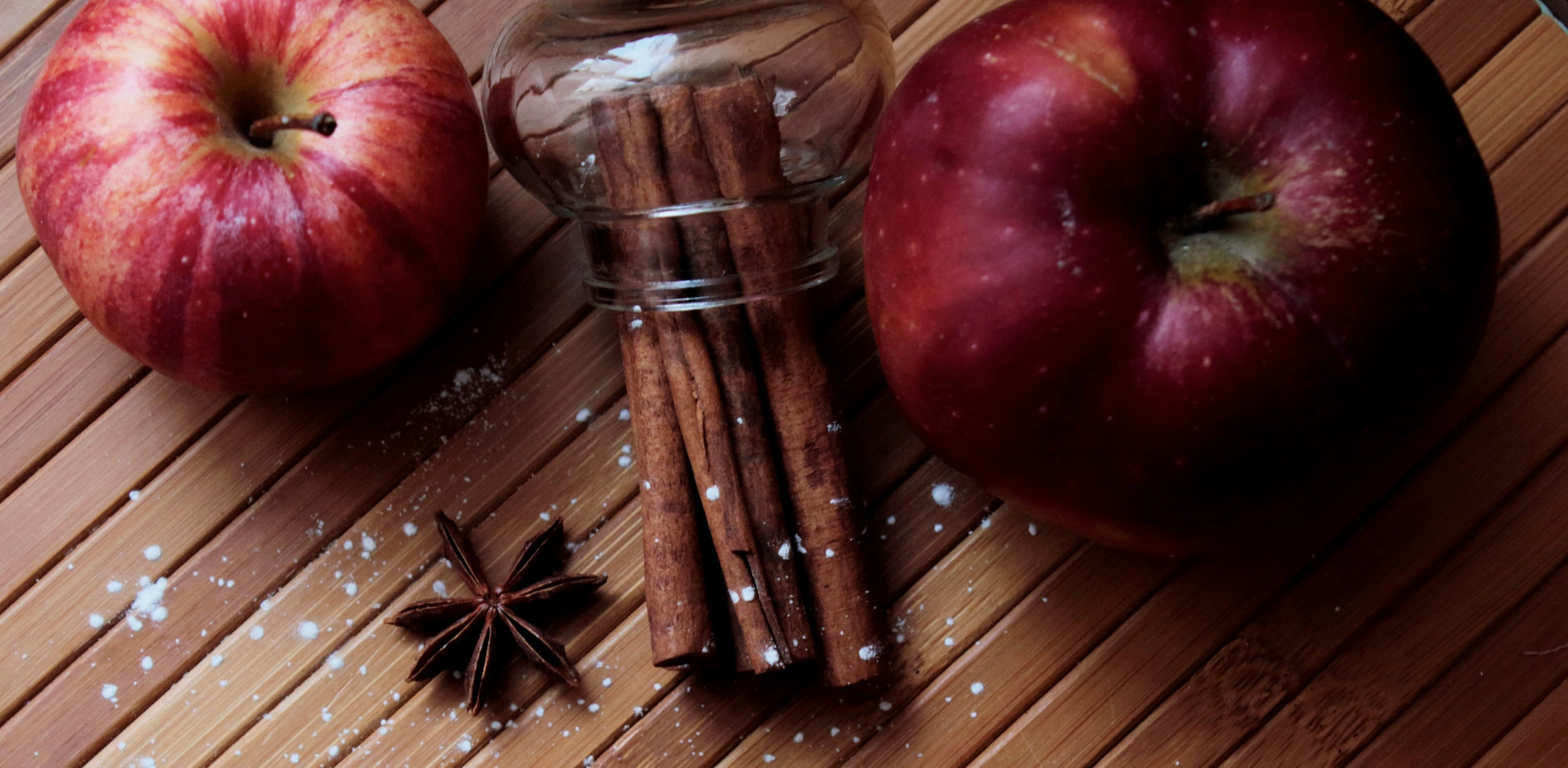 two apples on a wood table with cinnamon sticks and anise.