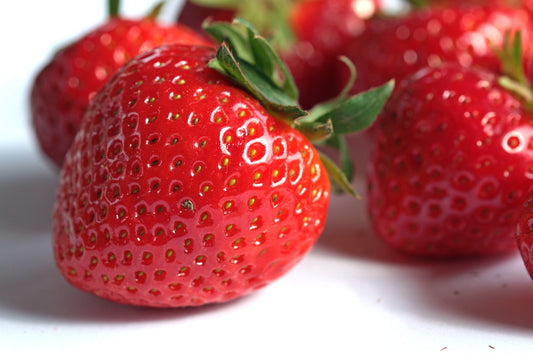Close-up of a red strawberry with green leaves on a white background