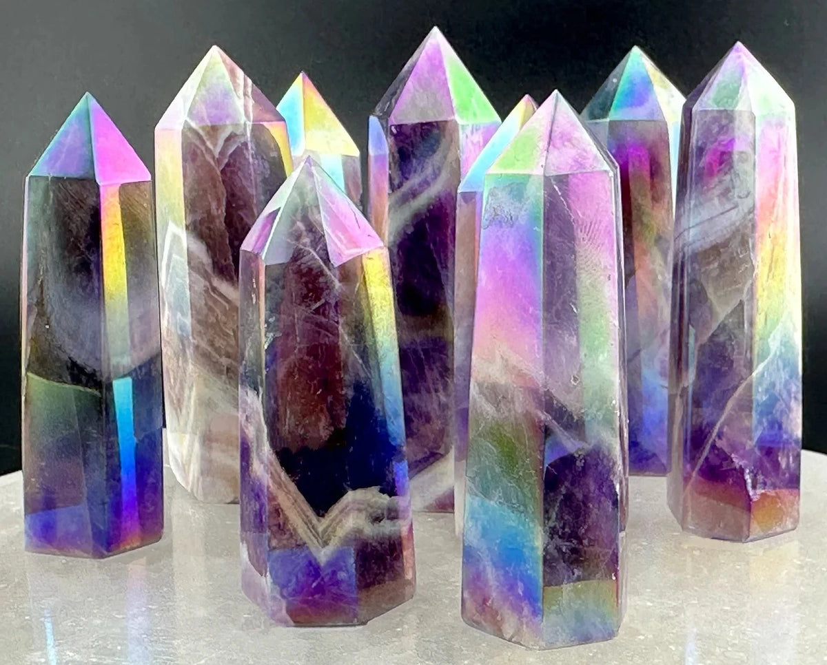 A set of tall, pointed iridescent crystal towers with purple, blue, green, and pink rainbow sheen, arranged on a light surface against a dark background.