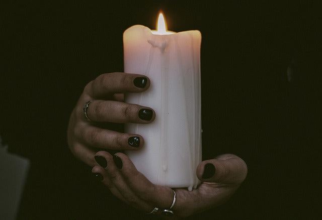 Two hands holding a lit white candle.