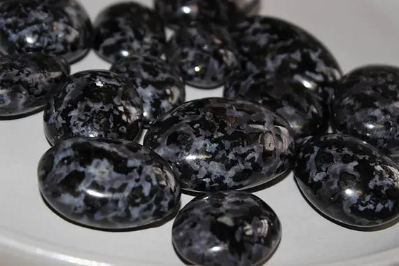 smooth, polished, ovular, palm sized stones, black, grey, and purple speckled stones with varying colour shades.