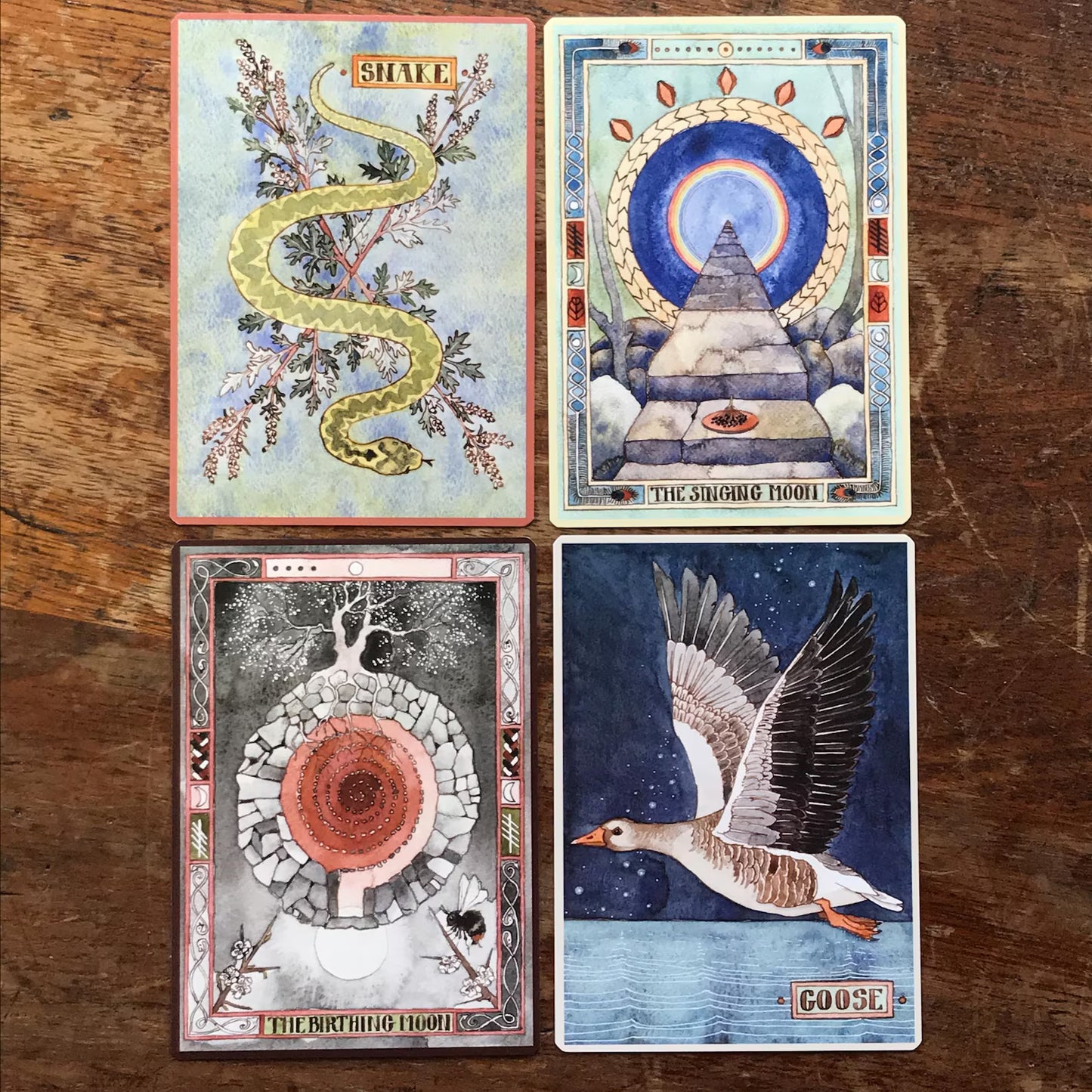 Four tarot cards with artistic designs on a wooden surface