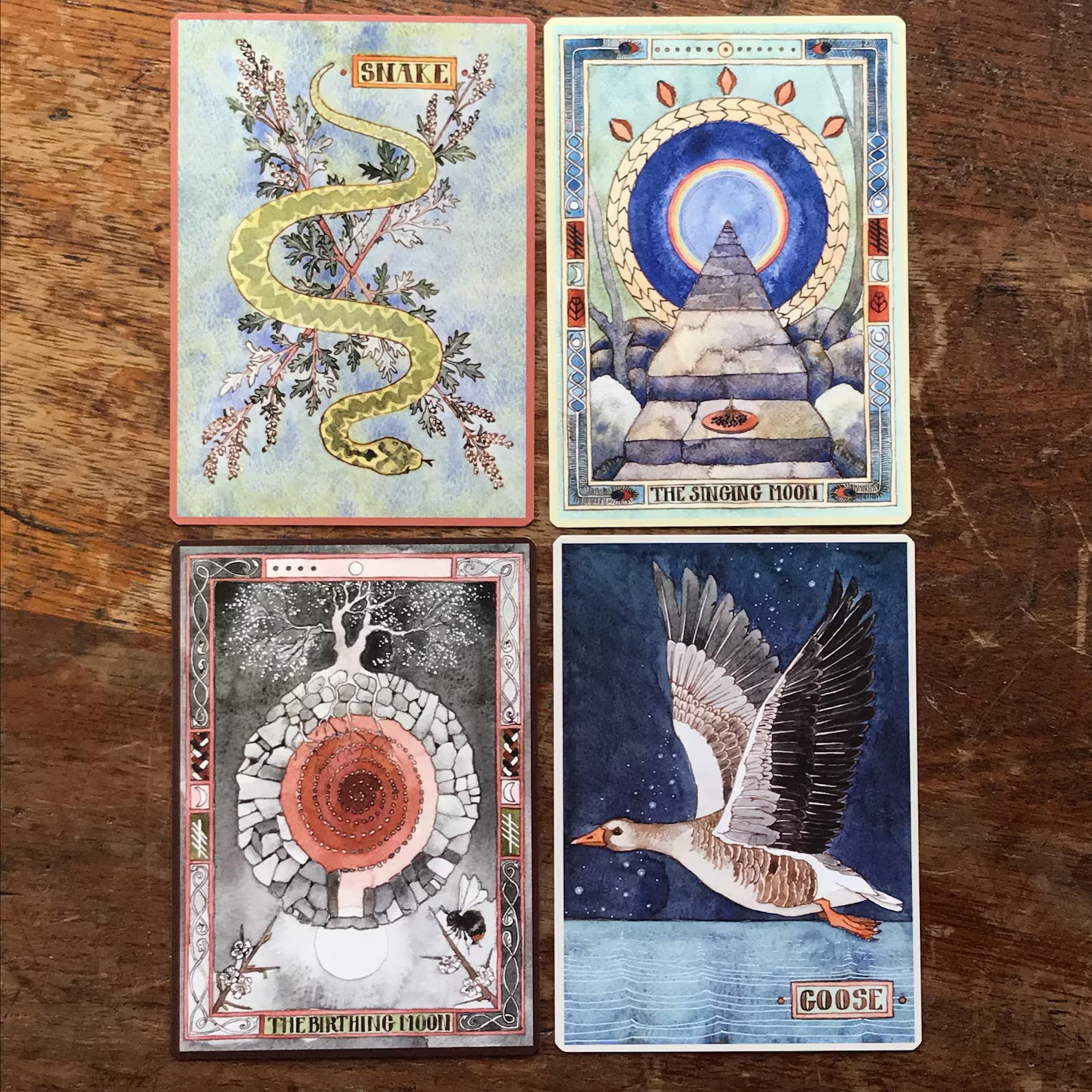 Four tarot cards with artistic designs on a wooden surface