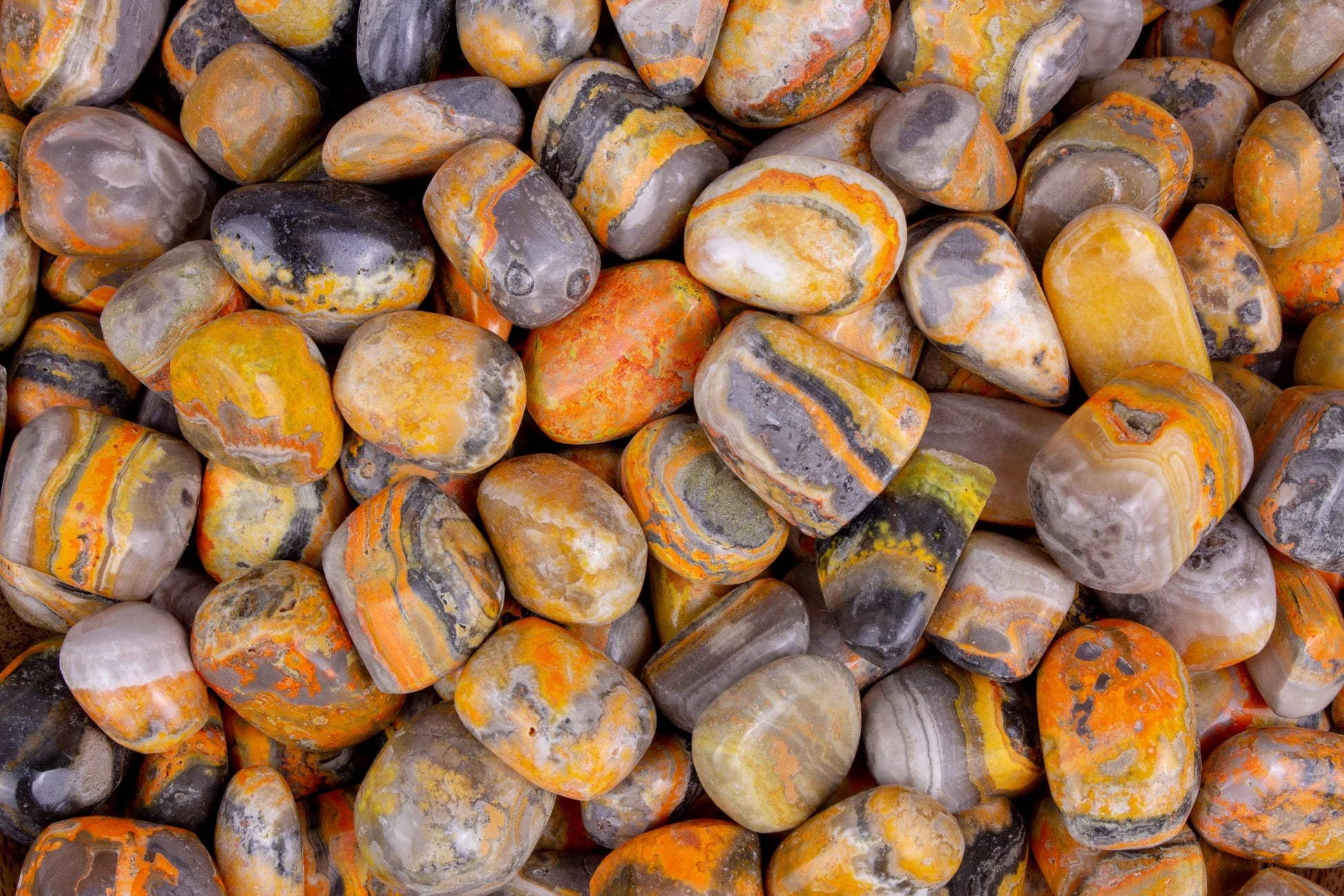 Smooth, tumbled, rounded rectangular stone, in banded layers of grey, white, yellow, and orange