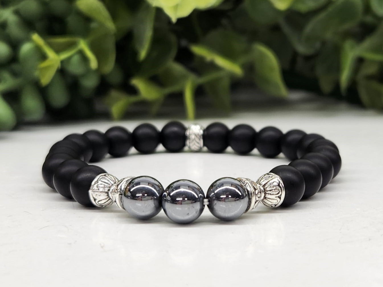 Black beaded bracelet with silver and gray beads on a light surface with greenery in the background