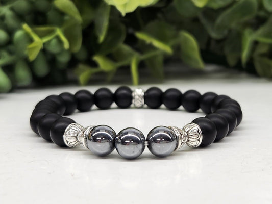 Black beaded bracelet with silver and gray beads on a light surface with greenery in the background